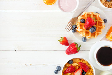 Wall Mural - Breakfast food side border. Fruits, cereal, waffles, yogurt and coffee. Top view over a white wood background with copy space.