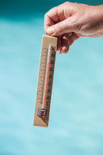 Closeup Of Wooden Thermometer In Hand In Border Swimming Pool