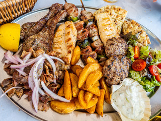 tasty dish with greek tzatziki sauce, a mixture of various types of grilled meat, chips and salad with onion and lemon for a meal