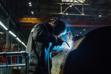 Wall Mural - Worker in protective mask welding pipe in factory