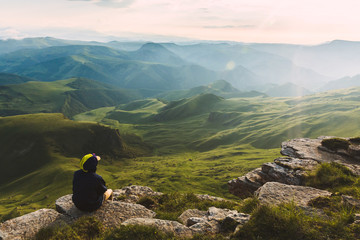 Travel man tourist sitting alone on the edge mountains over green valley adventure lifestyle extreme vacations green landscape Freedom