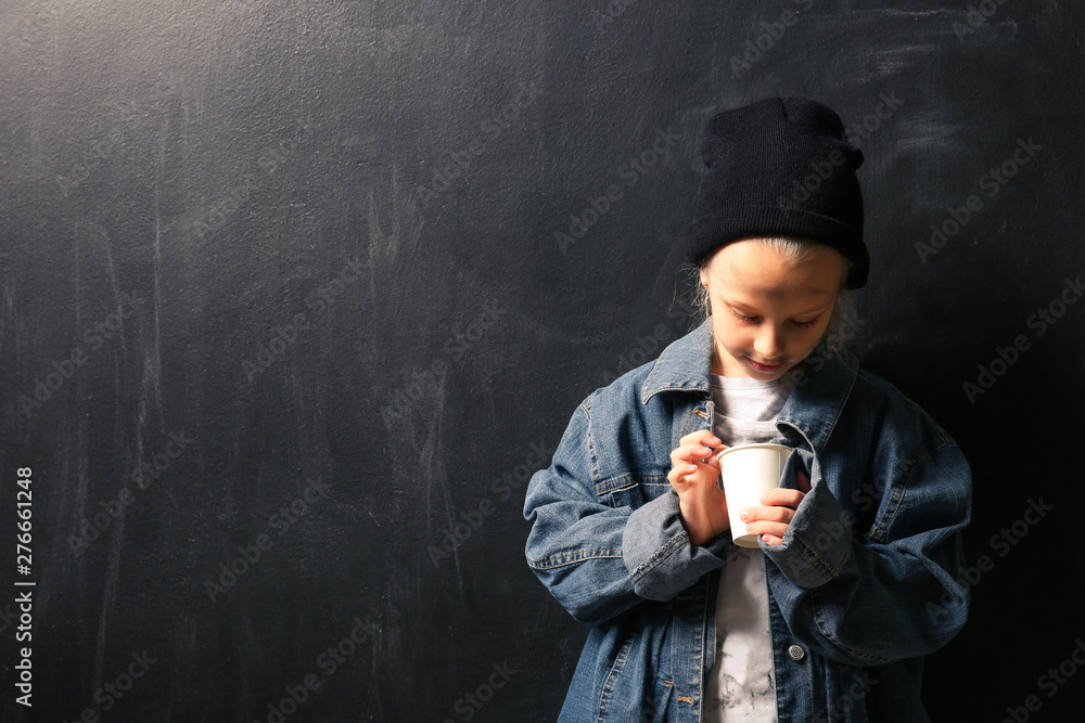 Homeless little girl with cup on dark background