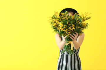 Beautiful young woman with bouquet of mimosa flowers on color background