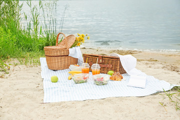 Wicker baskets with tasty food and drink for romantic picnic near river