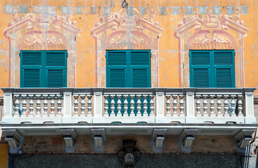 Canvas Print - Close-up of the balcony of an old villa in the historical centre of Rapallo with closed green shutters and multicolored trompe l'oeil decoration on the façade, Genoa, Liguria, Italy