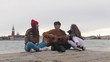 © KONSTANTIN SHISHKIN - A group of young friends sitting on the edge of the quay and singing songs by the guitar - Venice, Italy