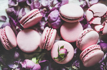 Sweet Pink Macaron Cookies And Lilac Rose Buds And Petals Over Wooden Background, Top View, Selective Focus, Close-up. Food Texture, Background And Wallpaper