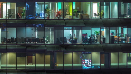 Wall Mural - Working evening in glass office building with numerous offices with glass walls and windows timelapse