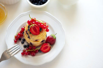 Wall Mural - Stack of pancakes (syrniki) with strawberry, red currant and blueberries on white backgraund. Soft focus. Healthy eating concept