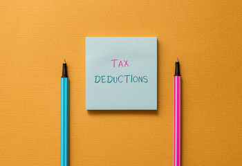 Text sign showing Tax Deductions. Business photo showcasing an amount or cost that subtracted from someone s is income Front view blank colored sticky note two ballpoints cool yolk background