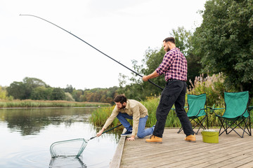 leisure and people concept - male friends with net and fishing rods on lake pier