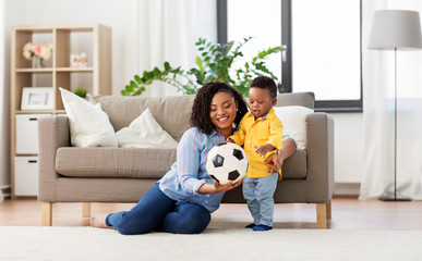 Wall Mural - childhood, kids and people concept - happy african american mother and her baby son playing with soccer ball together on sofa at home
