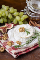 Wall Mural - fresh round cheese on linen napkin in white red cage, branch of green grapes in bowl of natural wood, slice of figs, rosemary