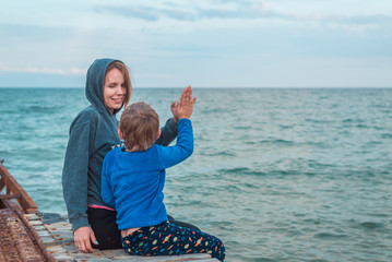 Mom and her little son are sitting together on the pier on the sea, the ocean and happily clapping each other's hands.