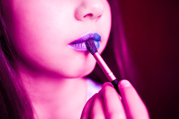 Girl in neon light with blue lipsteak on her lips.