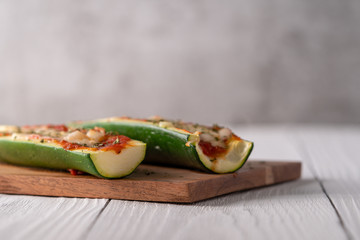 Two fresh hot zucchini boats with red sauce and melted cheese on cutting board.