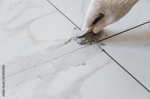 Grouting tiles seams with a rubber trowel.