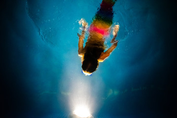 Mermaid diving towards the light of a blue pool at night, with a dreamlike background of fantasy and imagination.