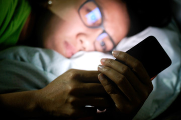 woman does not sleep and is stressed at night. She uses and looks smartphone in the bedroom without light and darkness.