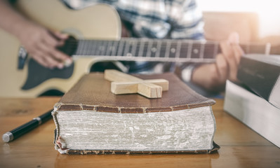 Wall Mural - Close up the old Bible and wooden cross with young male playing guitar acoustic at background. Christian worship God concept.