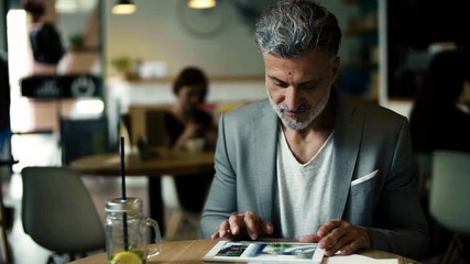 Wall Mural - A portrait of a mature businessman sitting in a cafe, using tablet.