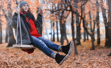 Girl in autumn city park in leaf fall. Young beautiful mother with her daughter on nature. A girl in a hat walks in the park.