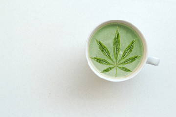 green leaf of hemp, marijuana in a white wide cup of green coffee