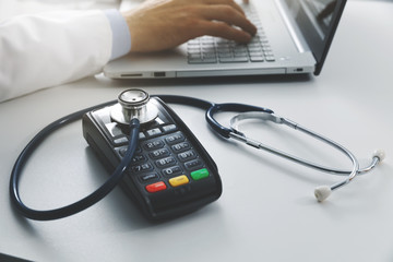 medical costs and health care expenses concept - payment terminal with stethoscope on the table in doctors office