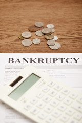 Sticker - selective focus of bankruptcy form, calculator and coins on brown wooden table