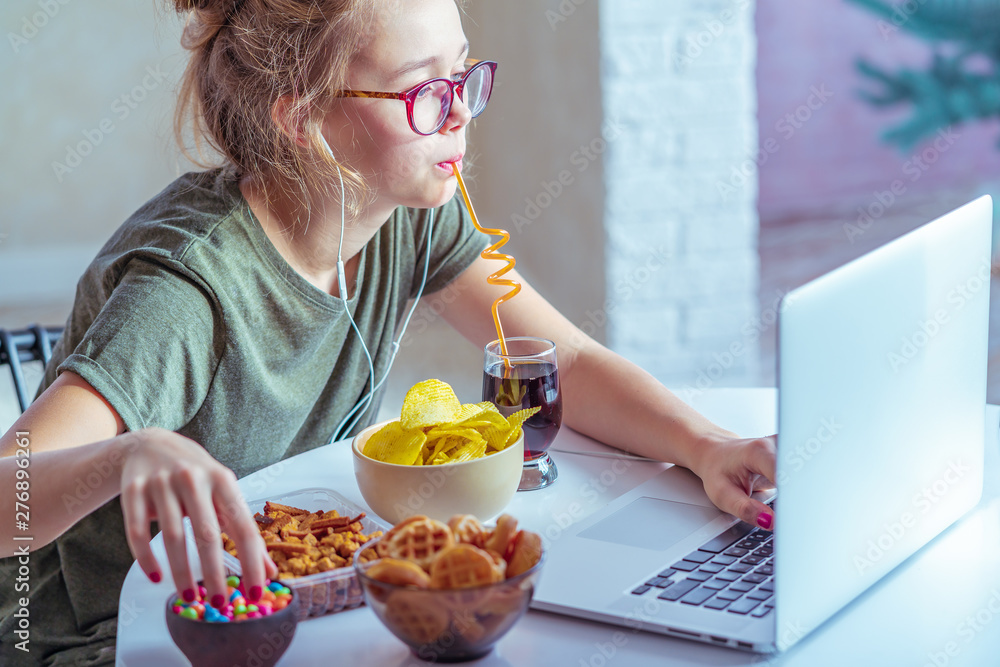 Girl works at a computer and eats fast food. Unhealthy food: chips ...