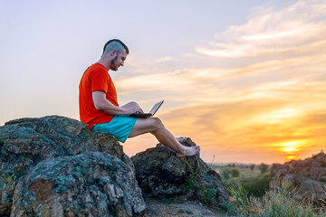 Business man working on a laptop while sitting on a rock, free space.