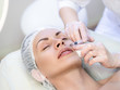 © junky_jess - Beauty injection. Female face in white cap and cosmetician hands with a disposable syringe. Correction of nasolabial folds. Selected focus