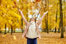 Season And People Concept - Happy Young Woman Throwing Maple Leaves And Having Fun In Autumn Park