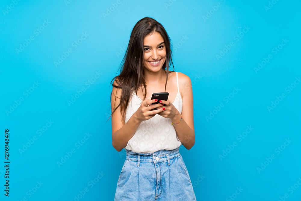 Young woman over isolated blue background sending a message with the mobile - obrazy, fototapety, plakaty 