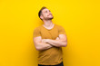 © luismolinero - Blonde man over isolated yellow wall looking up while smiling