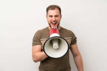 Handsome man over isolated white wall shouting through a megaphone