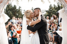 A Bride And A Groom Are Kissing In Front Of The Guests.