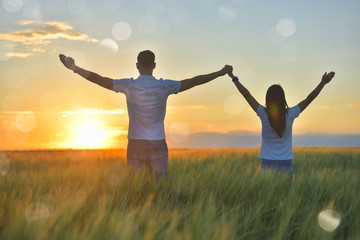 Wall Mural - Young couple feeling free in a beautiful natural setting, in what field at sunset