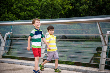 Wall Mural - Portrait of two boys kid a walk over a bridge and looking down, child walking outside in sunny day, Young boys relaxing outdoors in summer on glass bridge. Tourism concept