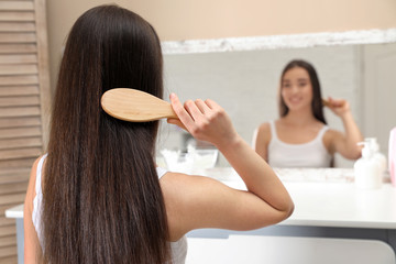 Wall Mural - Beautiful young woman with hair brush looking into mirror in bathroom