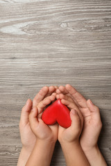 Woman and child holding heart on wooden background, top view with space for text. Donation concept