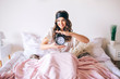 © estradaanton - Dark haired beautiful young brunette wake up in her bed. Cheerful nice woman holding clock in hands and smile. Look straight on camera. Sleeping mask on forehead. Positive happy model in bedroom.