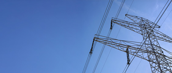 looking up steel power pylon construction with high voltage cables against blue sky. wide banner for