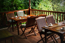 Empty Wooden Chairs And Tables, With Coffee Cups Upside Down - Ready For Morning Breakfast, Jungle Rainforest In Background