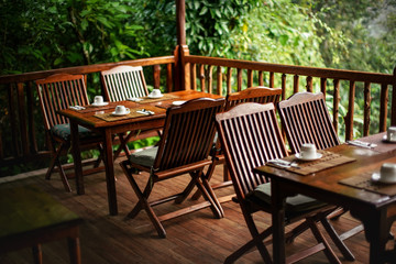 Empty wooden chairs and tables, with coffee cups upside down - ready for morning breakfast, jungle rainforest in background