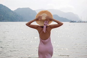 girl in straw hat and pink dress walking on the beach