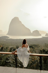 Woman with the white dress sit and see the mountain in early morning at the Sametnangshe Island viewpoint, Phang-Nga, Thailand.