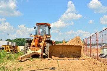 Wall Mural - Wheel loader bulldozer with bucket on a construction site. Clearing the ground for digging the foundation pit