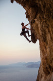 Fototapeta  - Young woman climbing challenging route at sunset