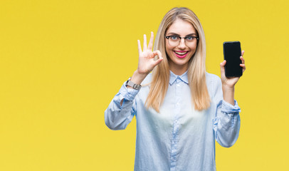 Sticker - Young beautiful blonde business woman showing screen of smartphone over isolated background doing ok sign with fingers, excellent symbol